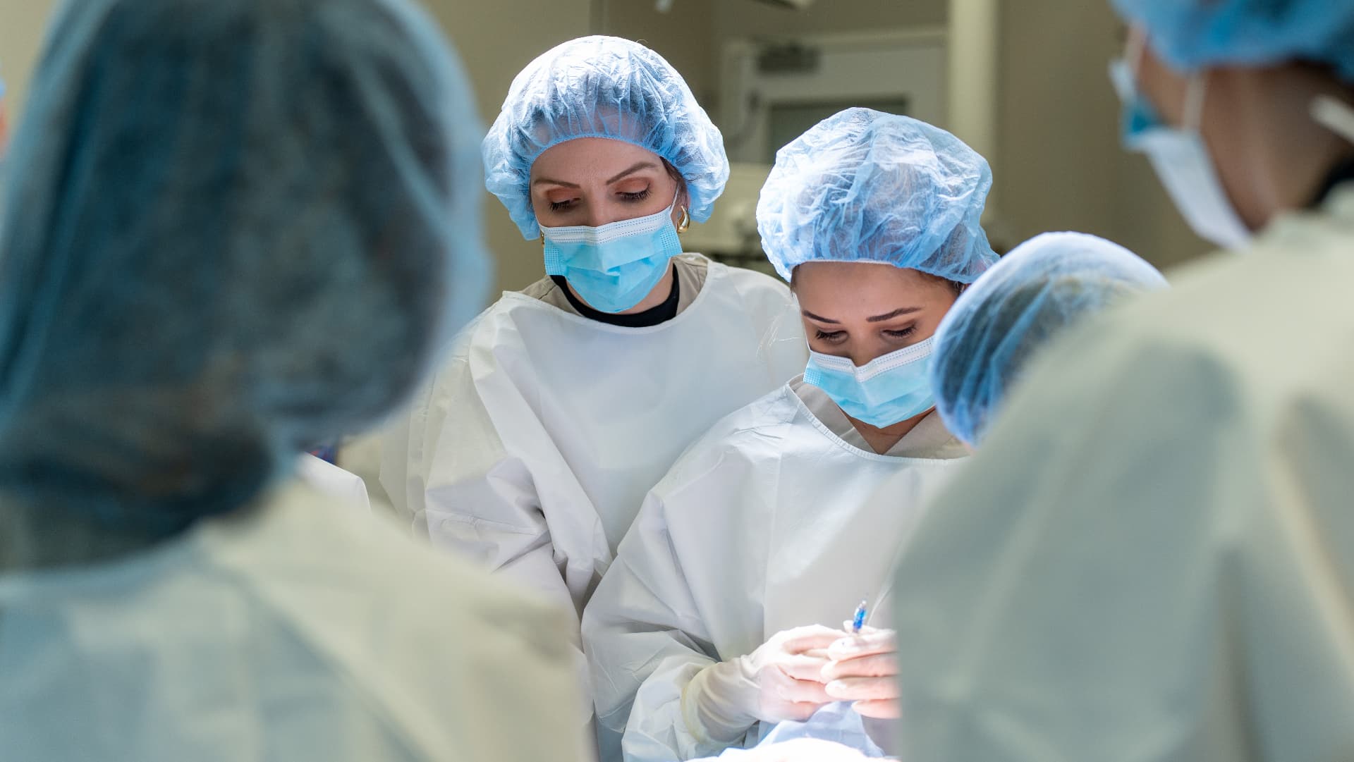 Two clinicians in gowns and masks working closely over a procedure table in a clinical training lab