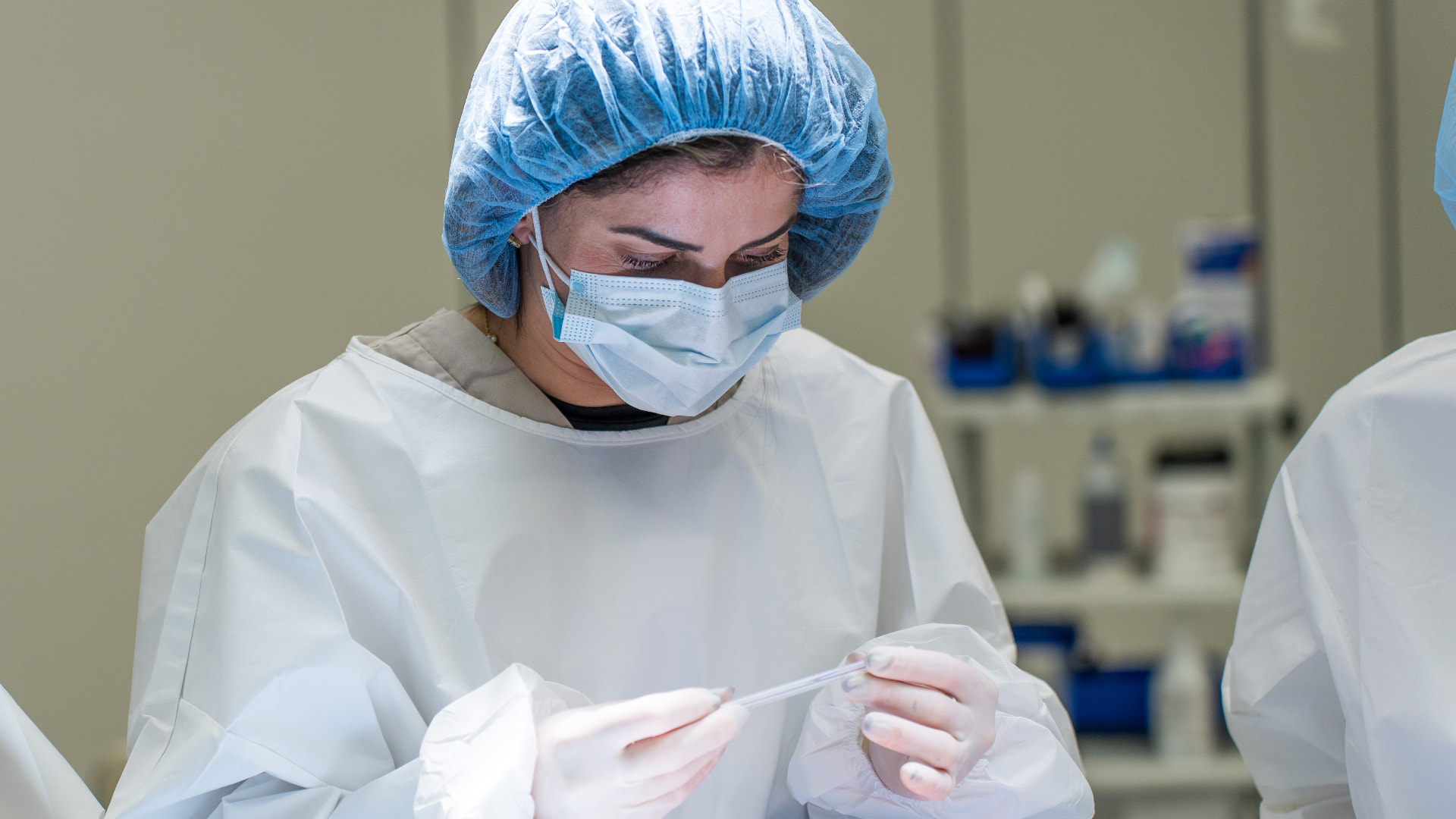 Clinician in surgical cap and mask carefully inspecting an instrument during a hands-on clinical lab