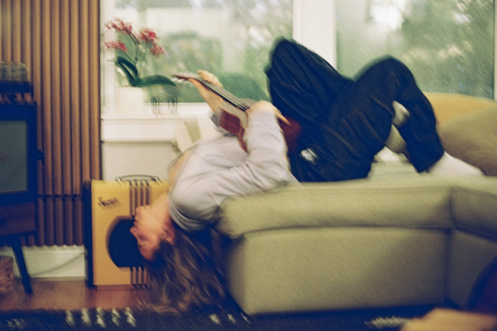 Motion-blurred film photo of a musician lying back across a couch while playing ukulele