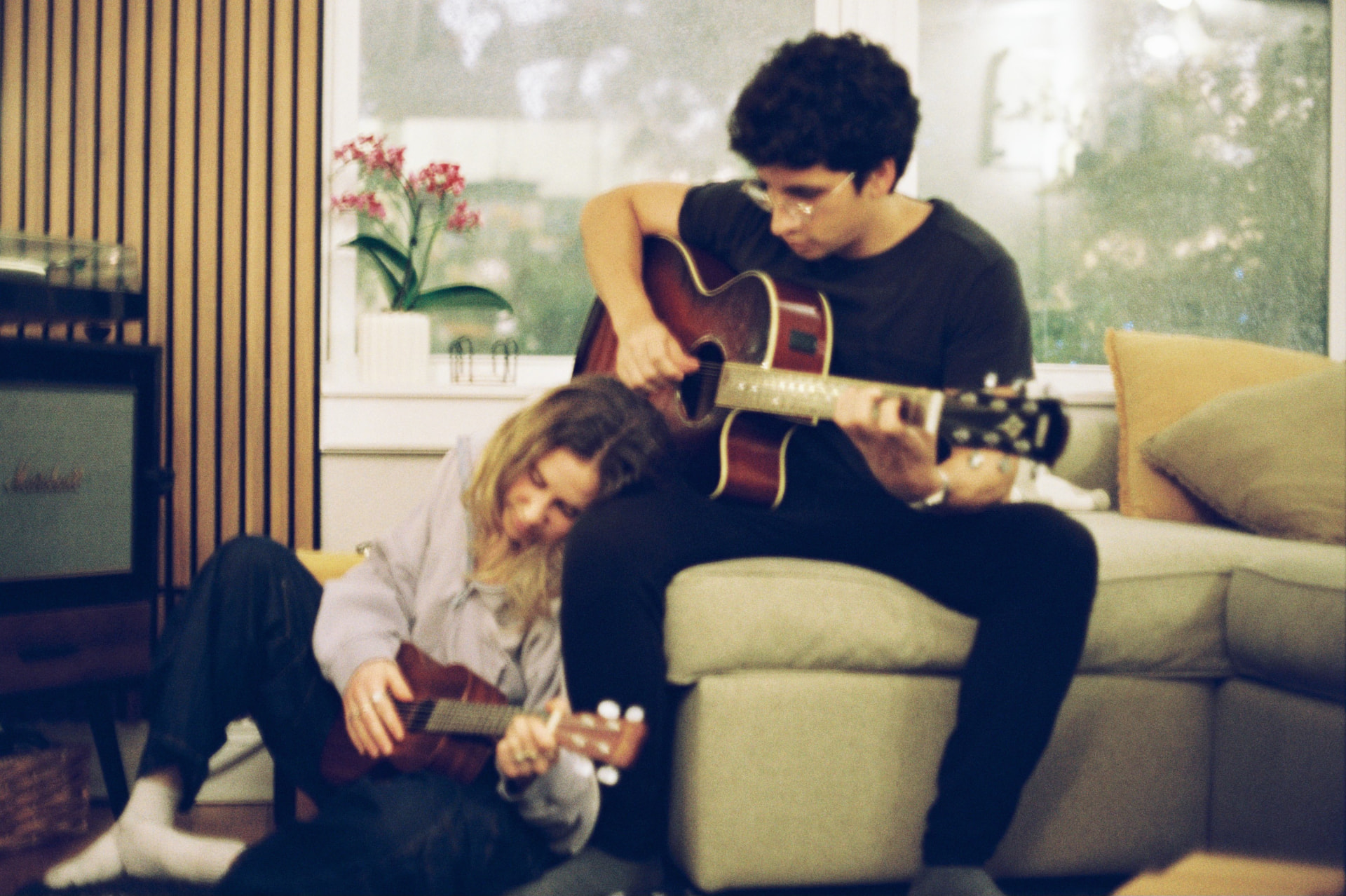 Film photo of two musicians playing guitar and ukulele together in a warm living room