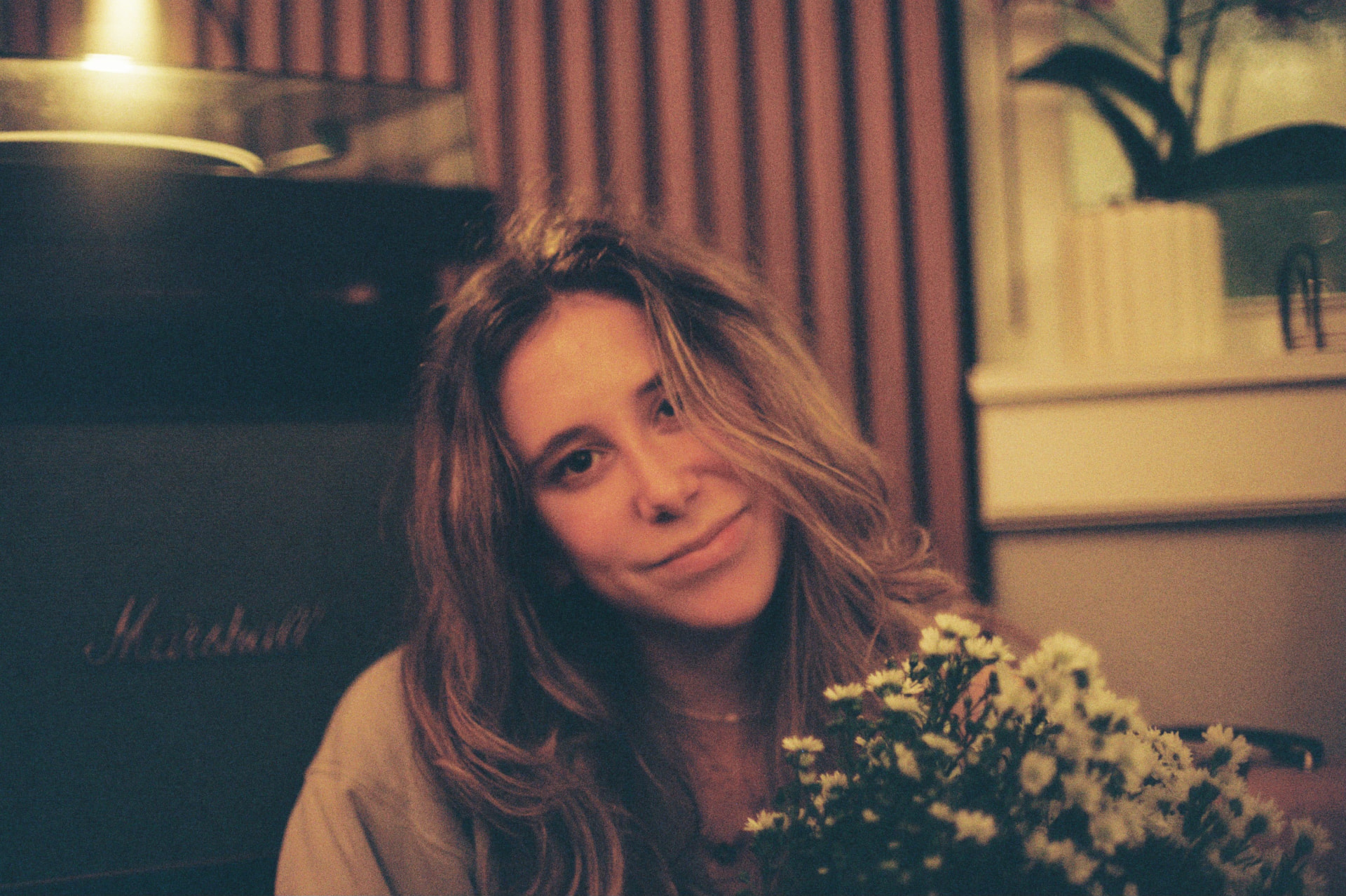 Warm film portrait of a woman beside a Marshall amp with white daisies in the foreground