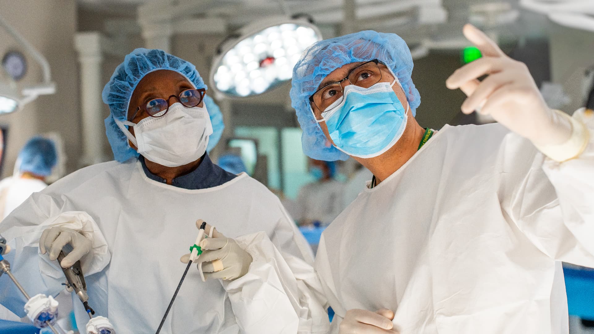 Two surgeons in scrubs and masks looking up at a monitor during a minimally invasive gynecologic surgery course