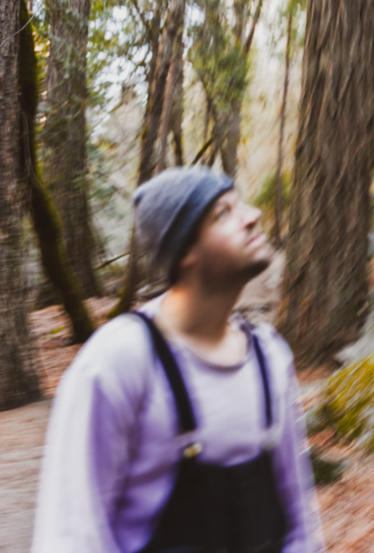 Motion-blurred portrait of a man in a beanie looking up among tall forest trees