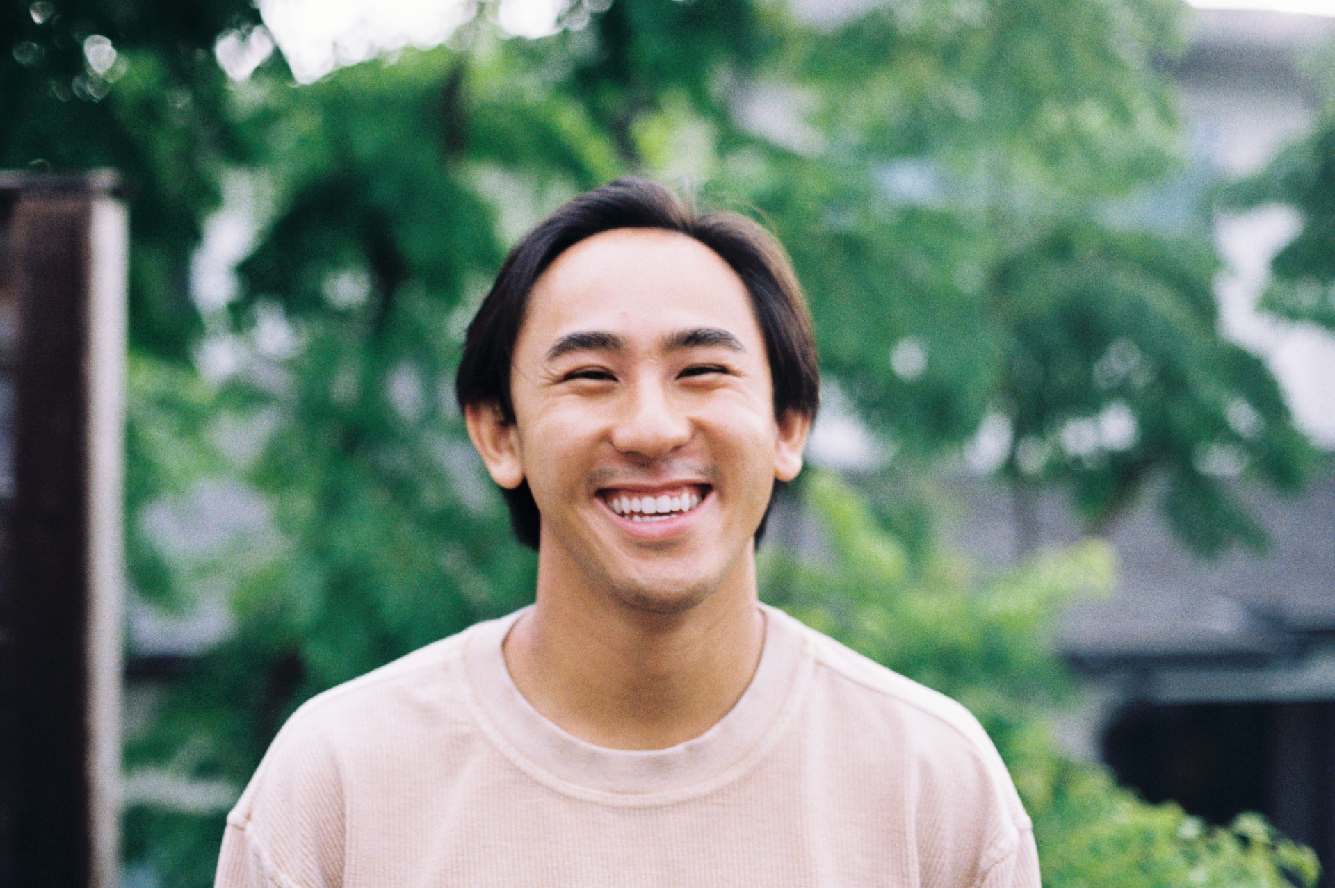 Portrait of a man laughing outdoors in front of green summer trees